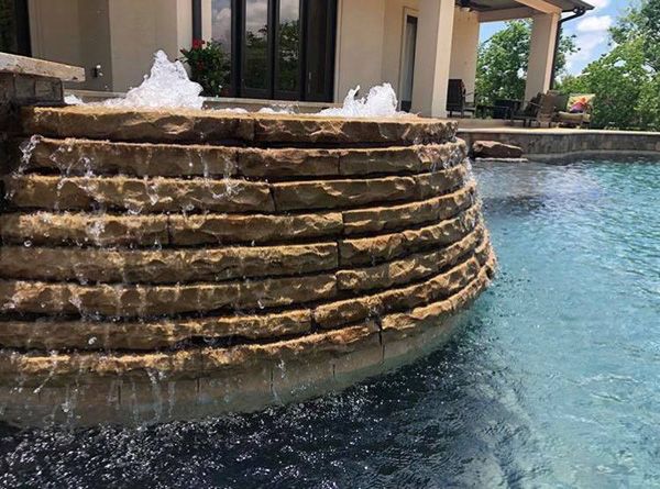 Tiered stone waterfall feature spilling into a Houston pool