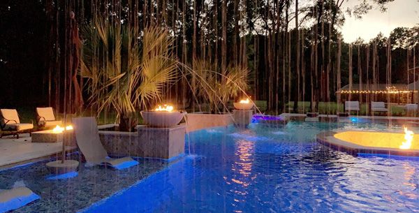 Houston pool lit at night with blue LED lighting and fire bowls on the deck