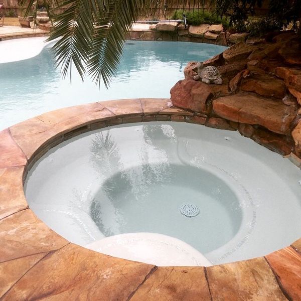 Freshly resurfaced round Houston spa beside a rock waterfall