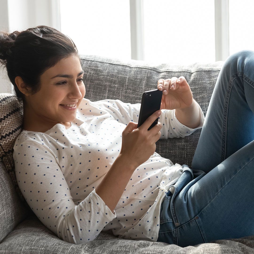 happy woman looking at her phone while sitting on a couch
