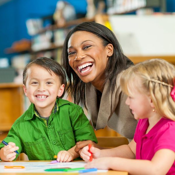 female teacher smiling while working with two students on their coloring