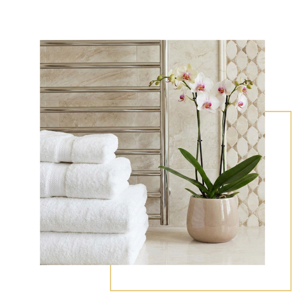 A stack of fluffy white towels on a heated towel rack next to a blooming orchid in a luxurious bathroom setting.