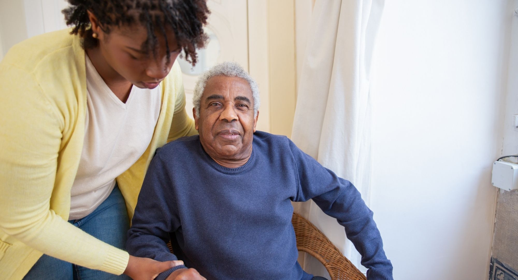older man sits in chair with person helping him older man sits in chair with person helping him