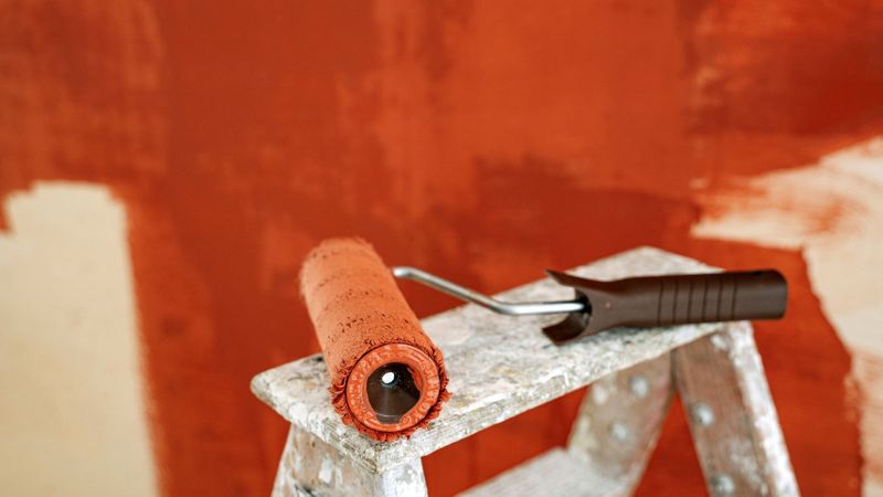 orange paint on walls with roller on ladder 
