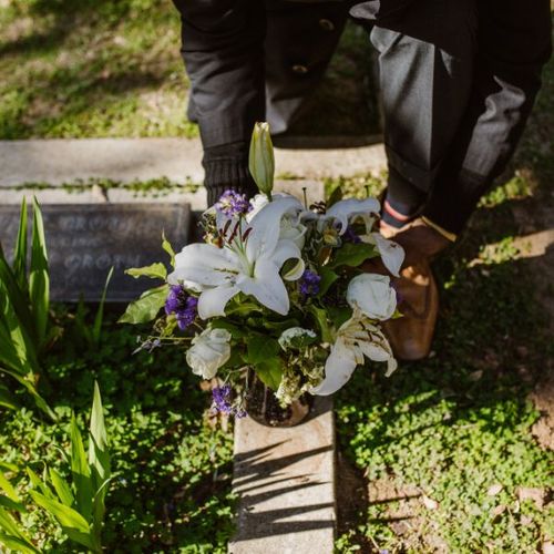 person placing flowers next to a headstone