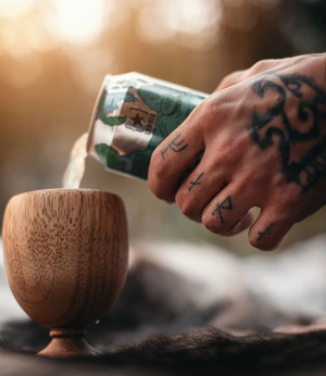 Tattooed Hand Pouring a Beer in a Wooden Cup.png
