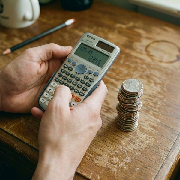 Hands holding a calculator next to a stack of coins.