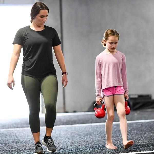 woman instructing a young girl through an exercise with weights