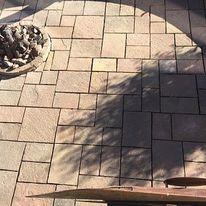 Overhead view of newly installed interlocking stone patio pavers in an earth-tone multi-size pattern, situated next to a stone-lined backyard fire pit feature. Brick Patio