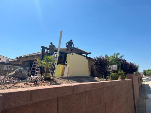 A new home construction site with a stucco wall and a patio cover being installed by a crew of workers stucco wall and a patio cover being installed