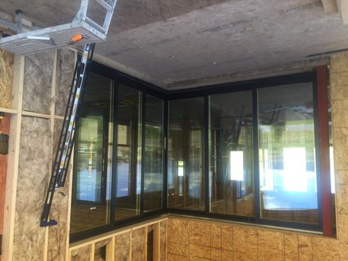 A professional installation of a floor-to-ceiling multi-panel glass window system in a luxury custom home. The image shows the industrial-grade black frames and high-efficiency glazing being fitted into the new construction residential frame. Installing large panel glass windows in Southern Utah