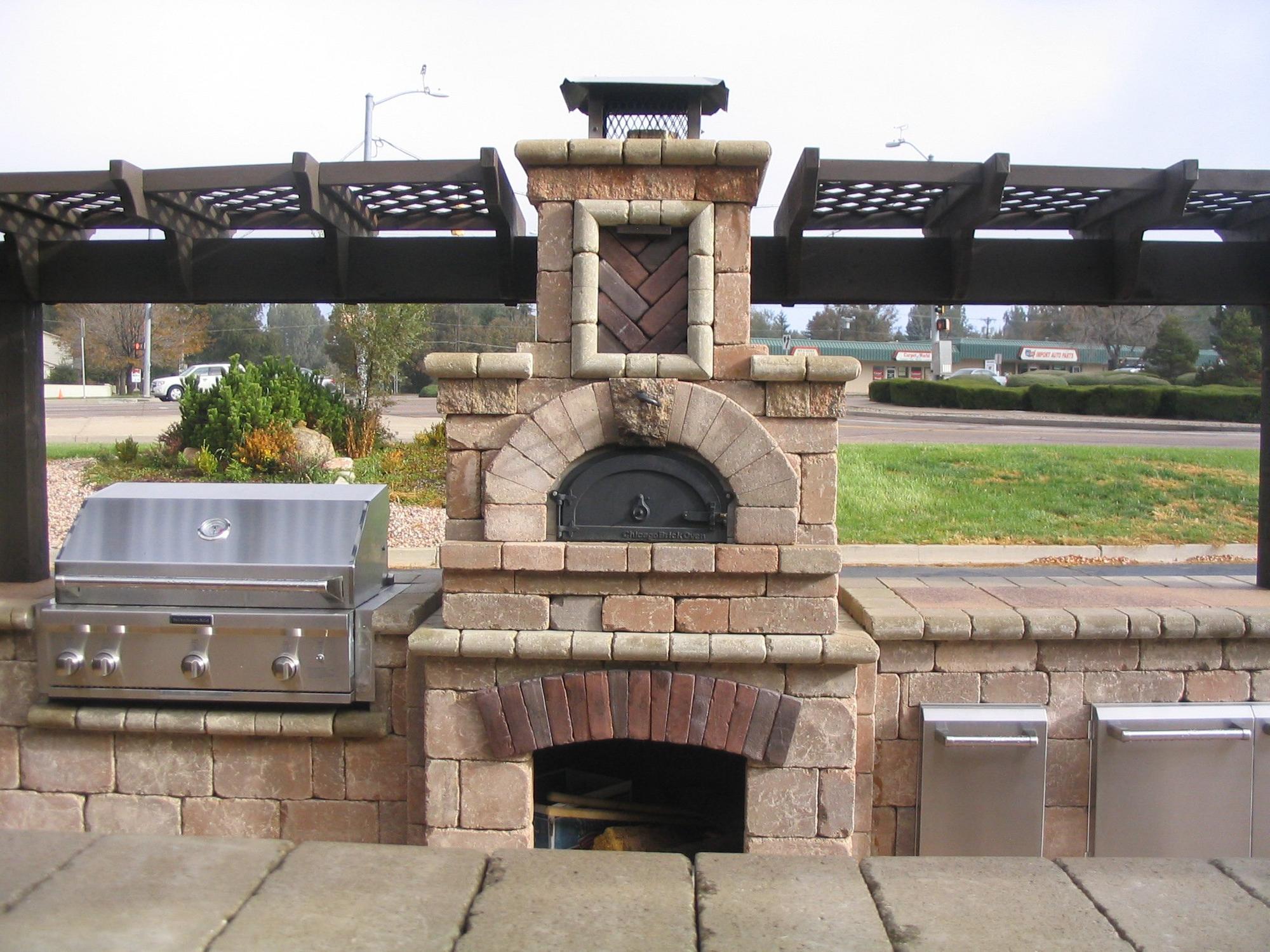 A custom outdoor kitchen with a built-in pizza oven, grill, and storage, constructed with stone masonry. Custom Outdoor Fireplace