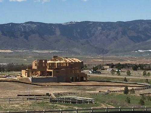 The intricate wood framing and roof trusses of a luxury residential estate under construction in Bloomington, Utah, showcasing the scale of the build against a mountainous desert backdrop. Custom home framing project in Bloomington Utah