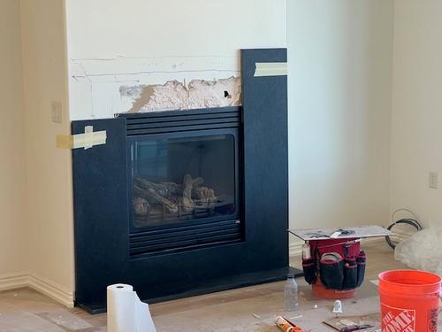 Progress shot of a modern gas fireplace receiving a dark stone slab surround. Fireplace Remodel Stone Installation