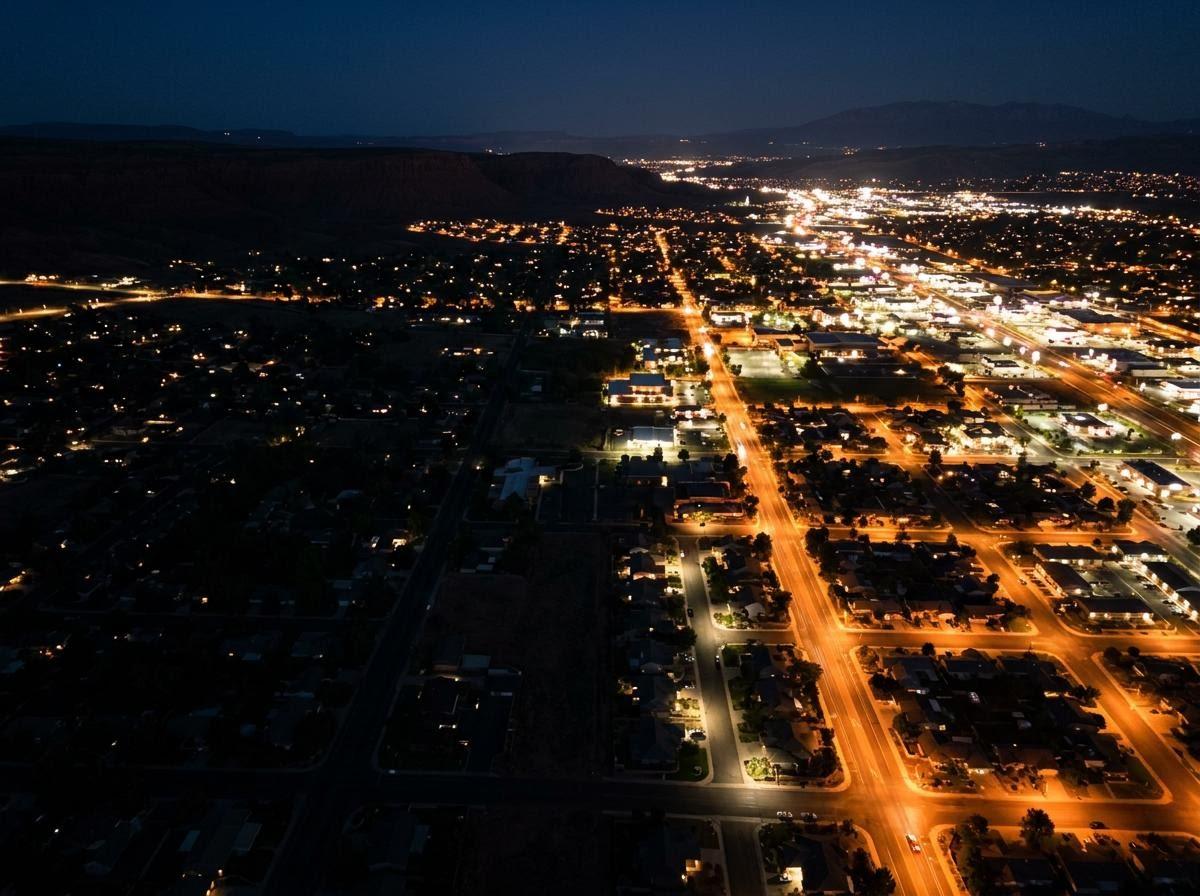 Aerial night photo of a lit St. George, Utah cityscape with residential areas contrasting with a commercial corridor, illustrating power grid stress. St. George City Lights at Night Aerial Grid Illustration