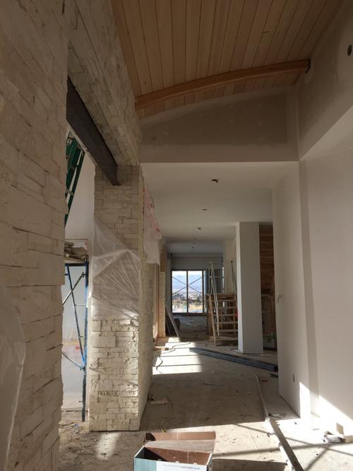 New home construction hallway in Southern Utah with a vaulted ceiling, exposed wood beams, and a modern stone wall House remodel