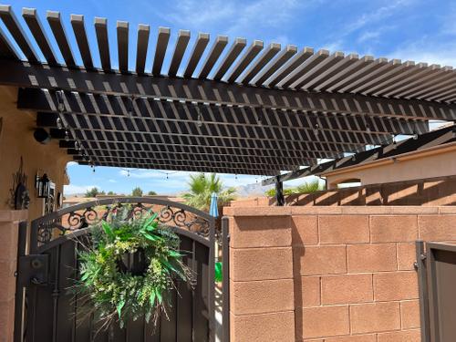 A newly installed pergola with a louvered roof, a wrought iron gate, and a wreath, providing patio shade. lattice pergola design