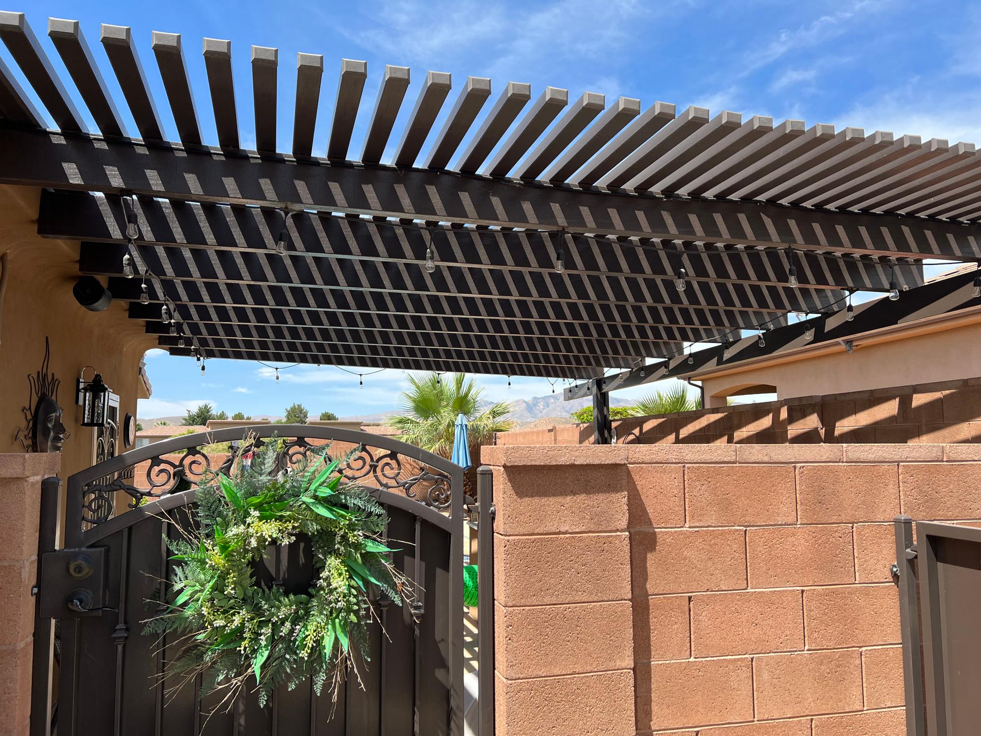 A newly installed pergola with a louvered roof, a wrought iron gate, and a wreath, providing patio shade. lattice pergola design
