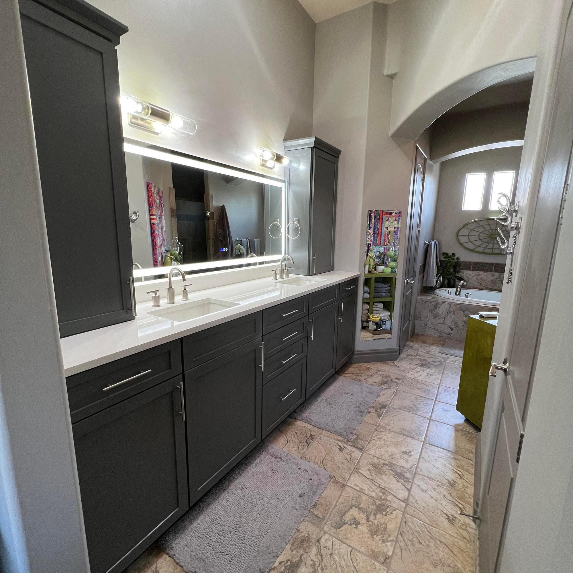 A modern bathroom remodel in St. George, Utah, with dark gray custom cabinetry, a lighted mirror, and a tile floor. Bathroom Remodel