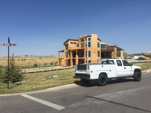 A wide-angle construction shot of a large custom home being framed with high-quality timber. The skeletal structure of the house is visible against a clear blue sky and red desert mountains, showcasing the early stages of a residential construction project in Southern Utah. Whole house wood framing in Utah desert