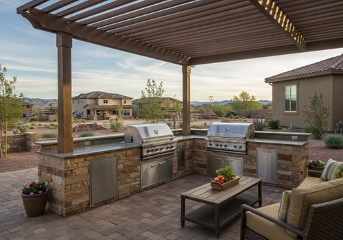 L-shaped outdoor kitchen island made of textured, earth-toned stacked stone beneath a slatted wooden pergola. The kitchen includes two separate stainless steel gas grills, an under-counter refrigerator, and storage drawers, connecting seamlessly to a paver patio seating area. Custom Built-In Outdoor Kitchen St George