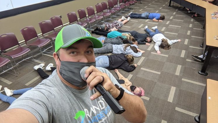 image of Randy Andrews talking into a microphone with hypnotised people sleeping on the floor 
