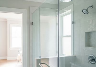Bright, accessible bathroom featuring a clear glass shower enclosure with a supportive handrail, tiled walls, a built-in niche, and a view to a sunlit room with a classic bathtub. Modern Bathroom with Glass Shower and Window