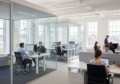 Bright and airy office featuring employees working at desks, some in glass-enclosed workstations, promoting collaboration and focus in a contemporary workspace. Modern Office Space with Glass Enclosed Workstations