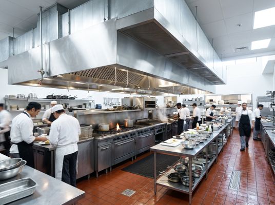 A pristine commercial kitchen environment showing stainless steel exhaust hoods above cooking equipment.