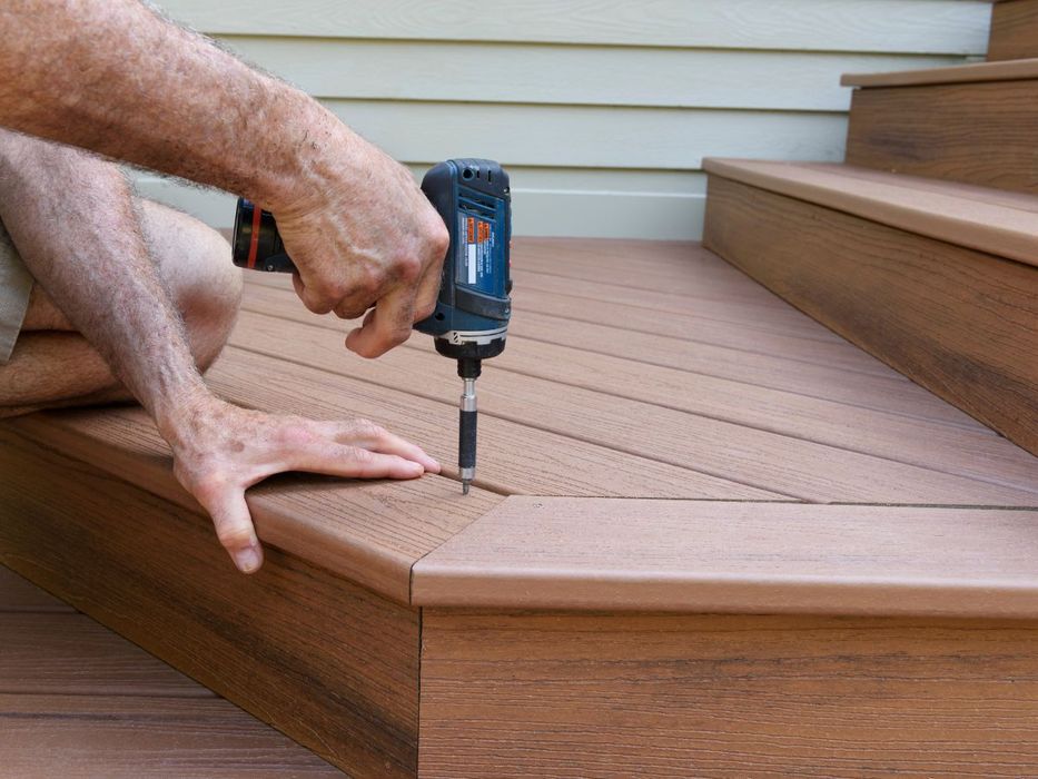 Image of a man using an electric screwdriver to drill in  a plank of wood to build stairs to a deck