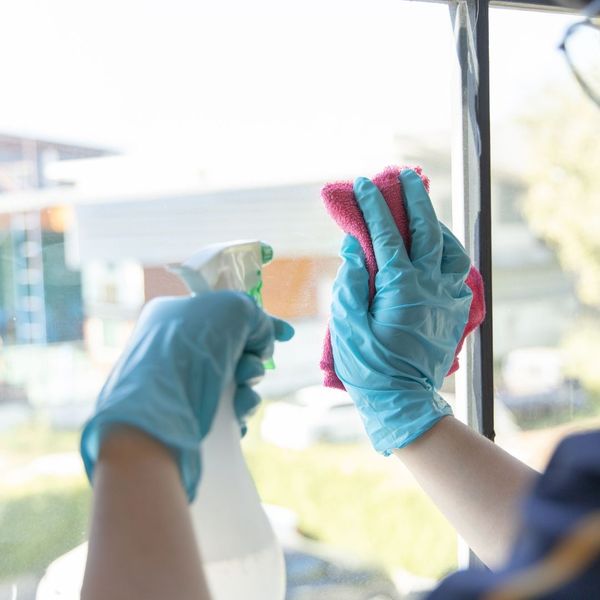 Hands in blue gloves are cleaning a window with a spray bottle and a cloth. Hands in blue gloves are cleaning a window with a spray bottle and a cloth.