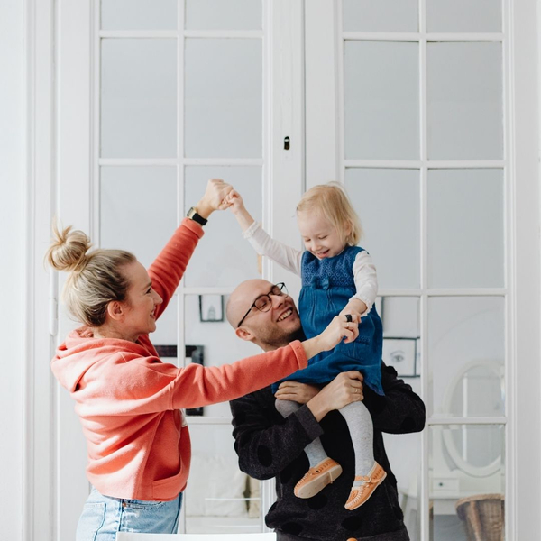 A smiling family of three plays together in a brightly lit room.