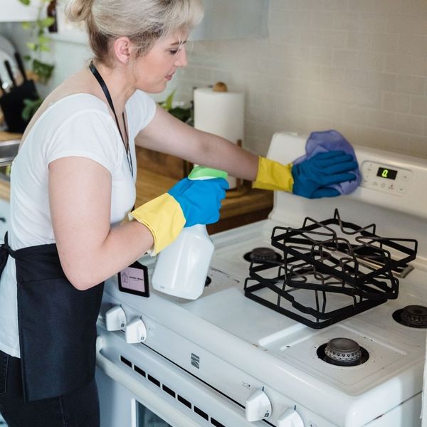 A person wearing gloves and an apron is cleaning a kitchen stove.