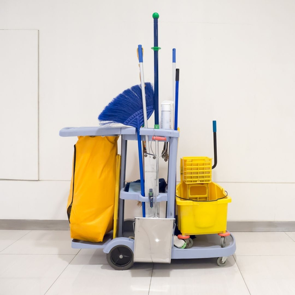 A janitorial cleaning cart filled with a broom, mop, and bucket stands in a hallway.