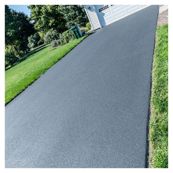 Freshly paved driveway beside green lawn and garage.