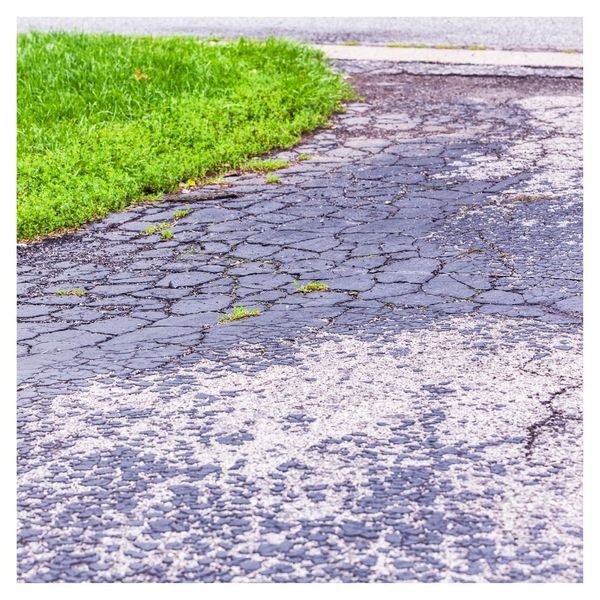 Cracked, weathered asphalt driveway with grass edge.