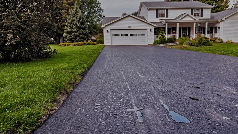 Wet asphalt driveway leading to a two-story house and garage.