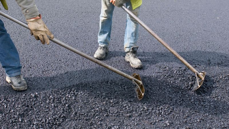 Two people finishing paving asphalt