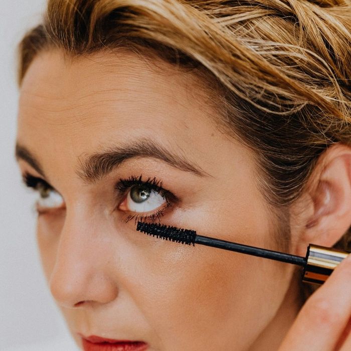 Woman applying black mascara to her lower eyelashes.