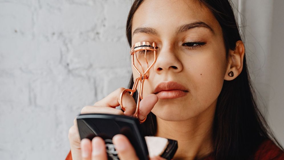 Woman using a rose gold eyelash curler. Woman using a rose gold eyelash curler.