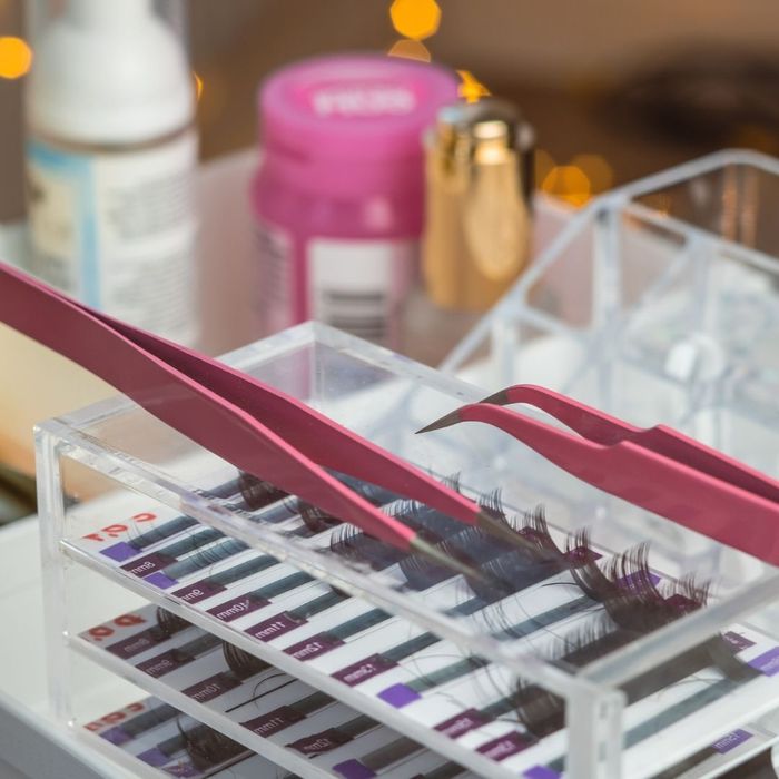 Pink tweezers resting on an eyelash extension organizer.