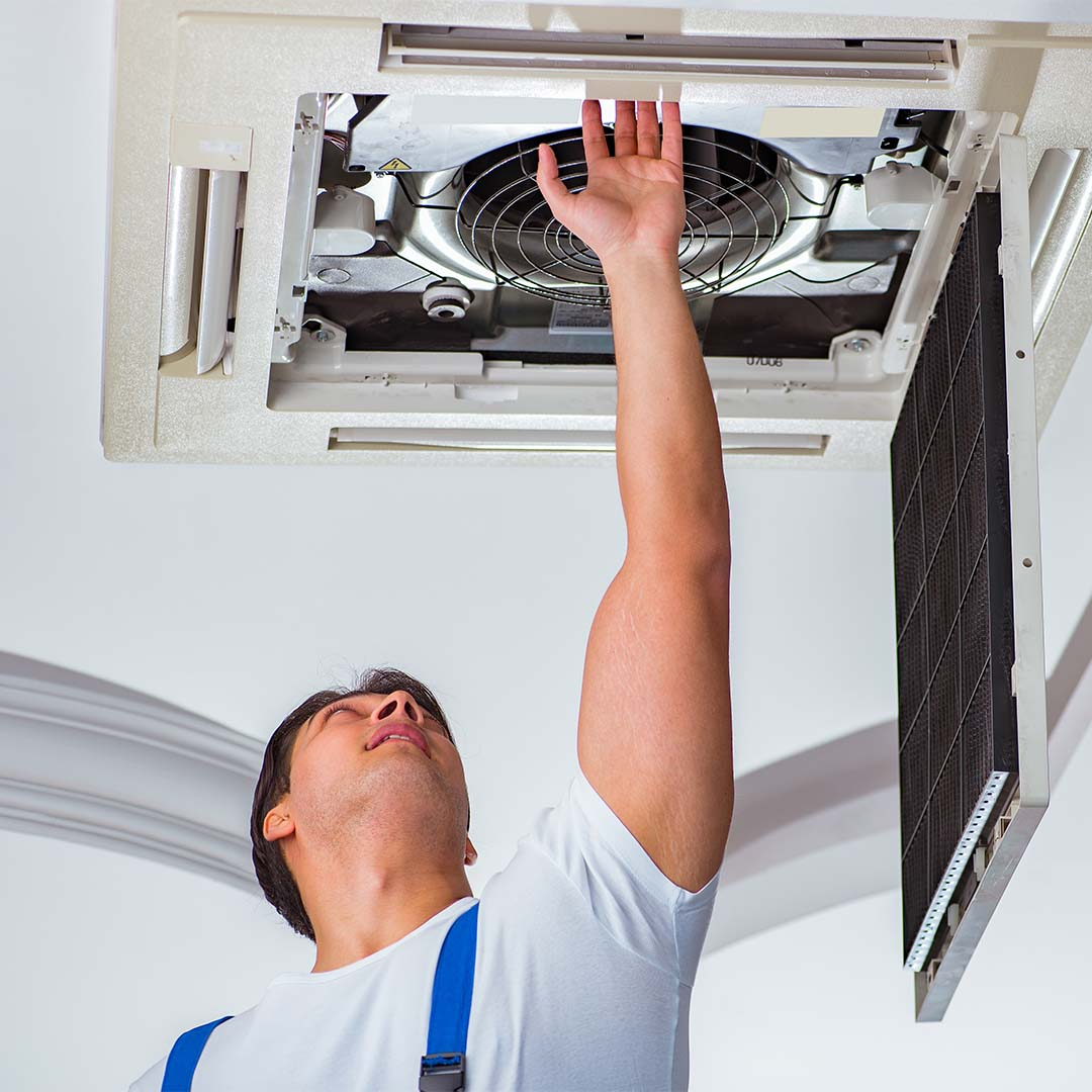 HVAC worker reaching up to open duct to repair it