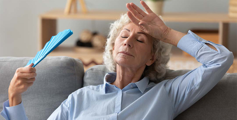 Older lady with fan trying to keep herself cool in home