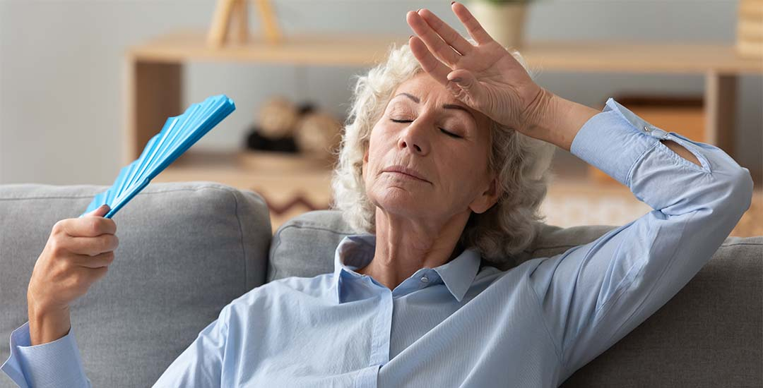 Older lady with fan trying to keep herself cool in home
