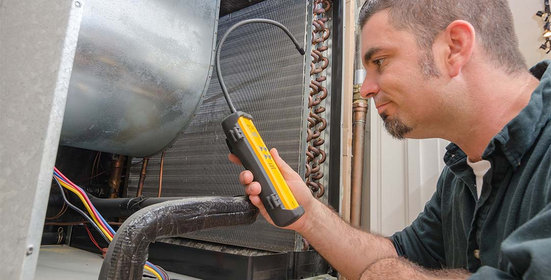 HVAC worker using leak detector on unit