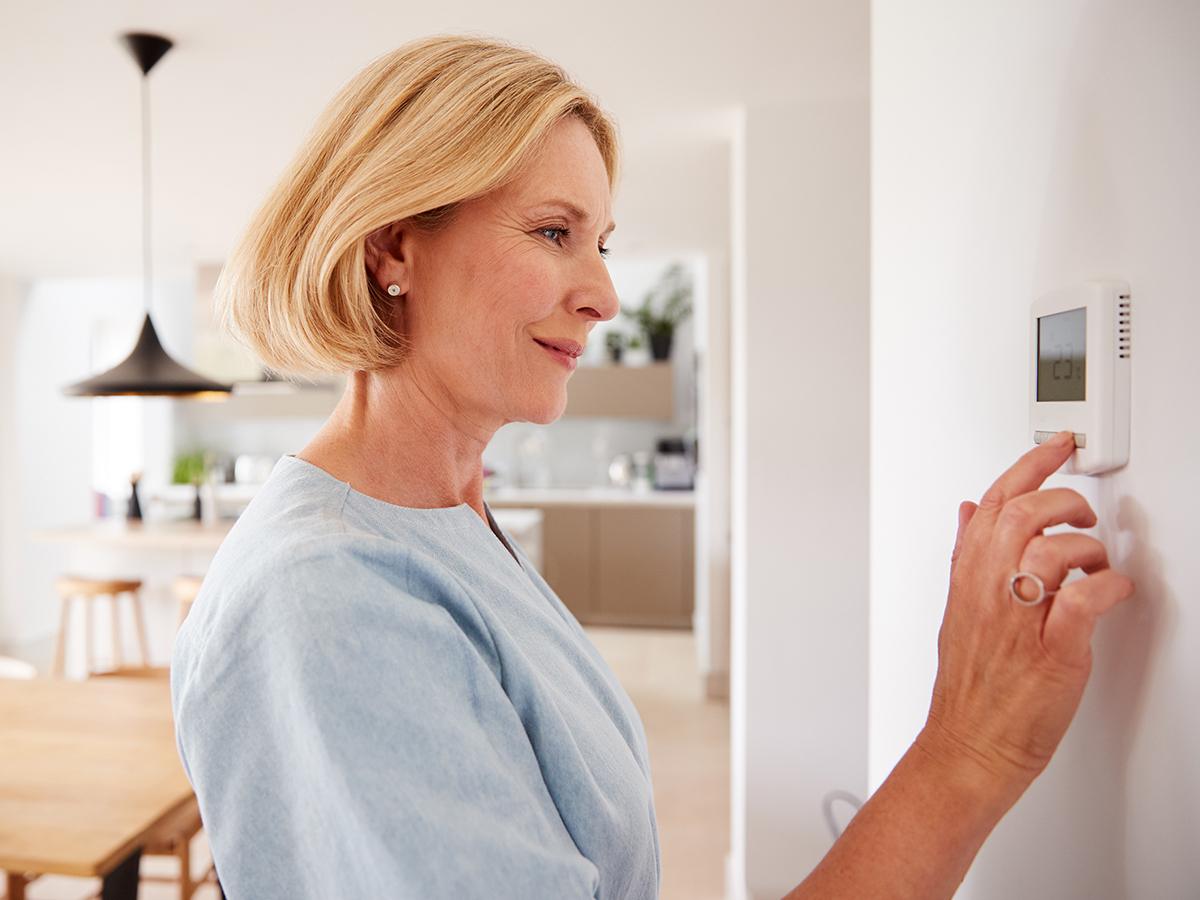 Woman checking a thermostat in her home