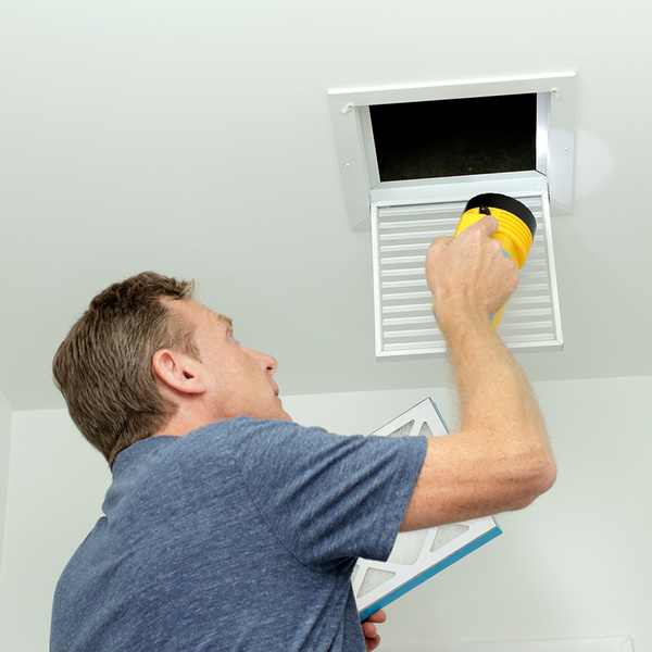 man shining flashlight into air vent