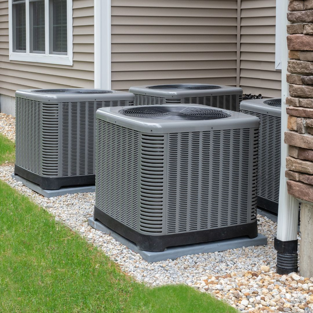 Four residential air conditioner condenser units outside a home