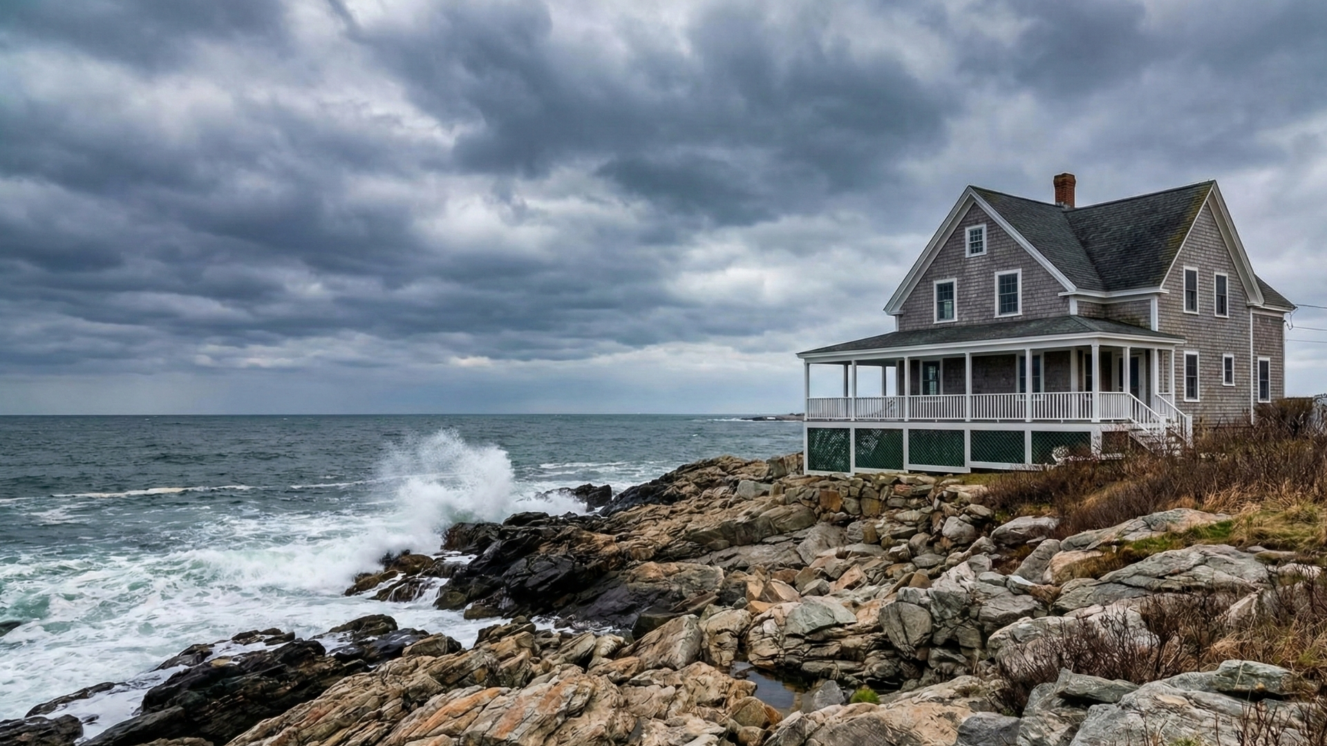 New England coastal house on a rocky shore under a dramatic, cloudy sky