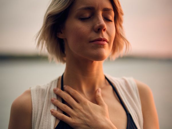 woman with hand over heart in meditation on the beach